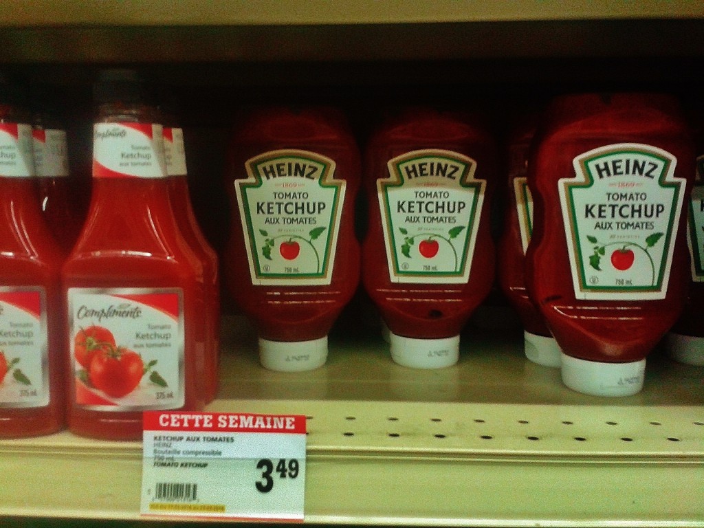 Heinz ketchup on the shelf (and on sale) at an IGA store in Quebec.  Made in Leamington, Ontario from local tomatoes until 2014.  The IGA store brand "Compliments" is to the left of Heinz.  Photo by James Morgan