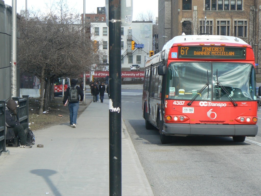 A homeless man sits on the Mackenzie King Bridge in downtown Ottawa while an OC Transpo bus passes.  The 2016 budget has measures to help the homeless and public transit.  Photo by James Morgan