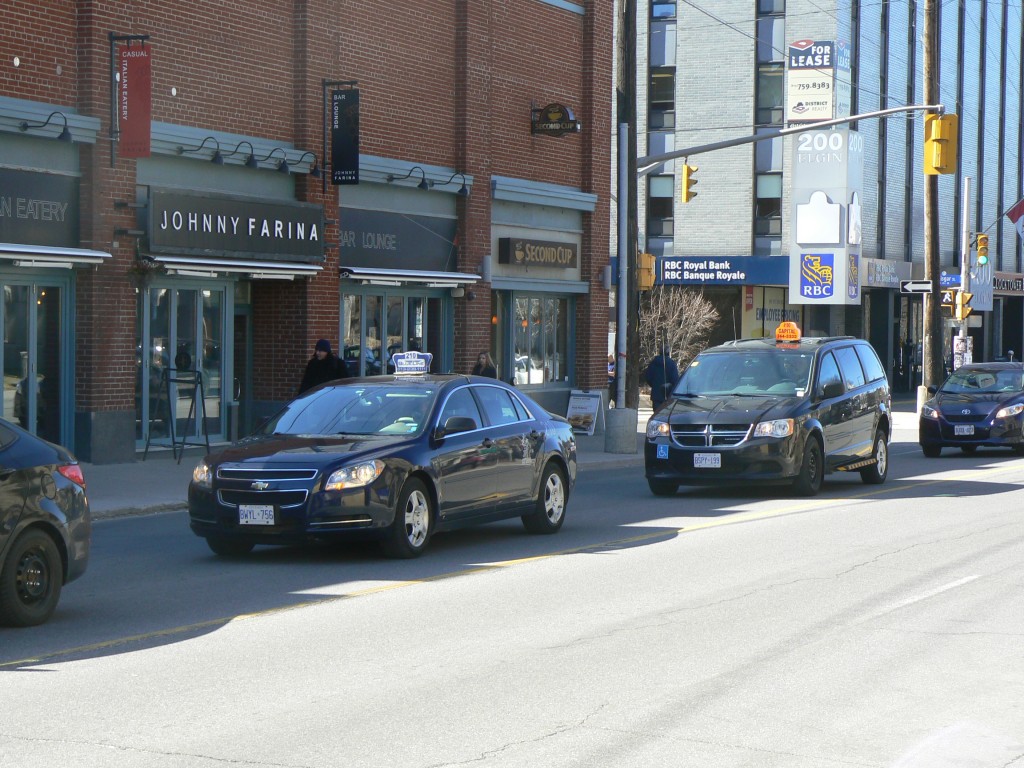Blue Line (front) and Capital (back) taxi cabs head south on Elgin Street in downtown Ottawa.  Both are facing stiff competition from Uber.  Photo by James Morgan