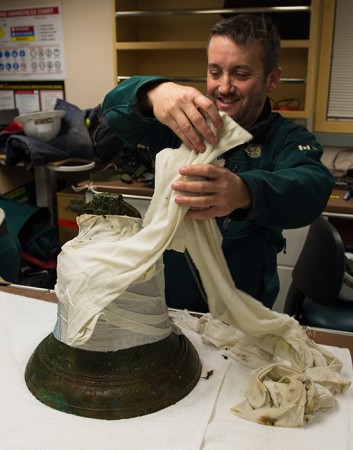 Parks Canada’s Jonathan Moore unwraps the ship’s bell of HMS Erebus in a lab aboard the Canadian Coast Guard Ship Sir Wilfrid Laurier.  © Parks Canada / Thierry Boyer